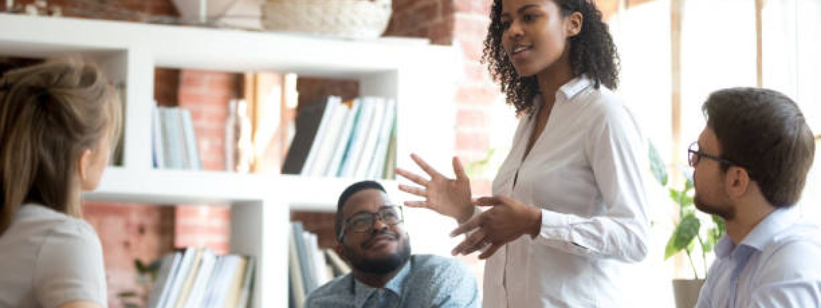 Ambitious smart african black female employee speaking at diverse meeting share creative idea opinion at group briefing while jealous envious skeptical male coworkers looking listening to colleague